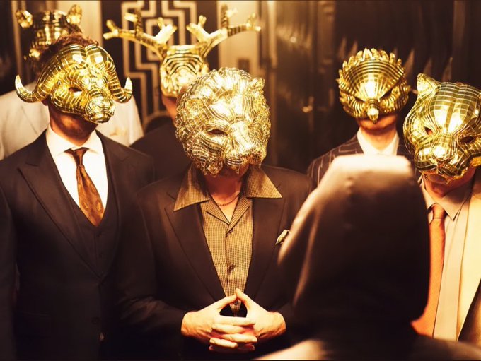 A group of people in business suits wearing ornate golden animal masks, with one person in a black mask holding their hands together.