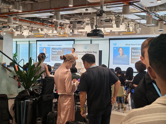 Attendees gather at the Animoca Portfolio Day event, held alongside Token2049, watching a presentation titled "Reimagining future economies" and "What hasn't changed" displayed on large monitors in a bright, modern venue.