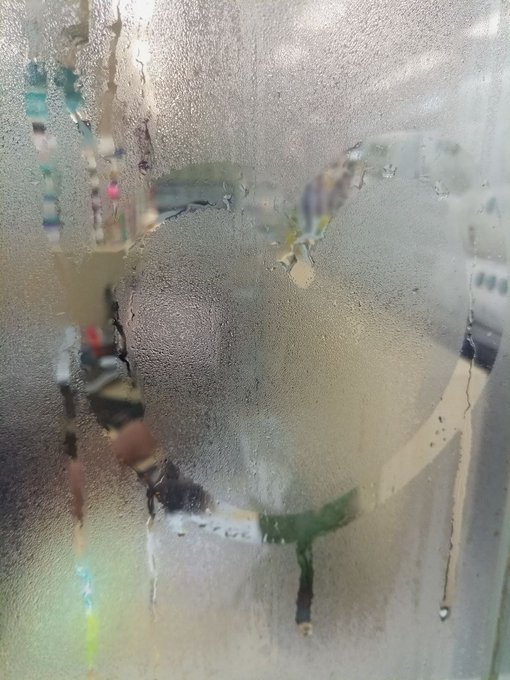 A heavily obscured, foggy, and water-streaked view through a glass surface, showing indistinct shapes and colors that make the scene difficult to identify.