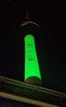 A tall tower illuminated in bright green light stands against a dark night sky.