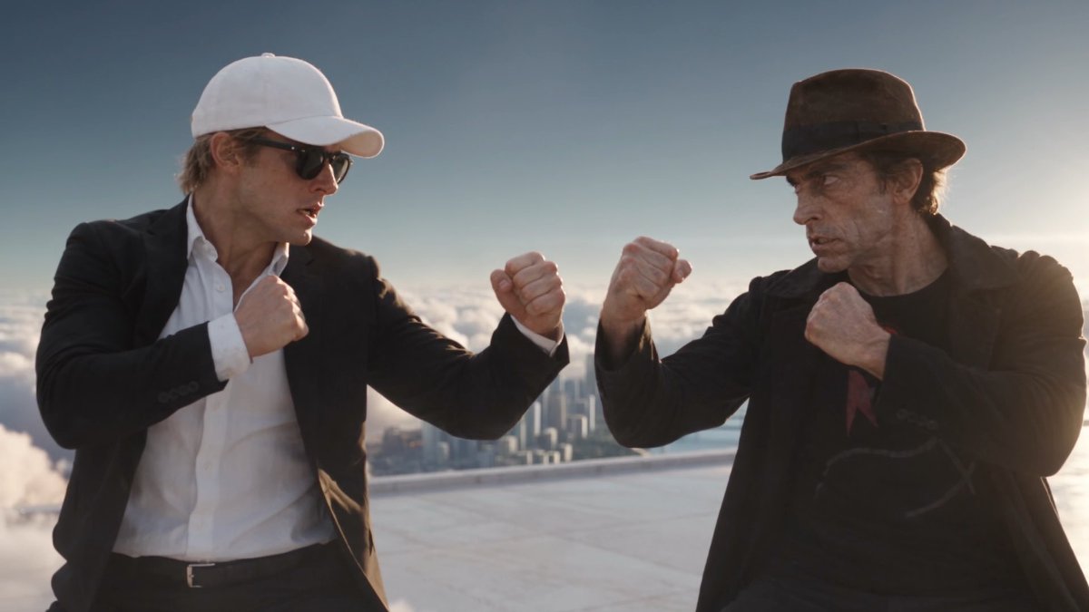 A scene from the movie 'Indiana Jones' showing two men in a fighting stance on a rooftop above the clouds, one wearing a white cap and the other wearing a brown fedora.