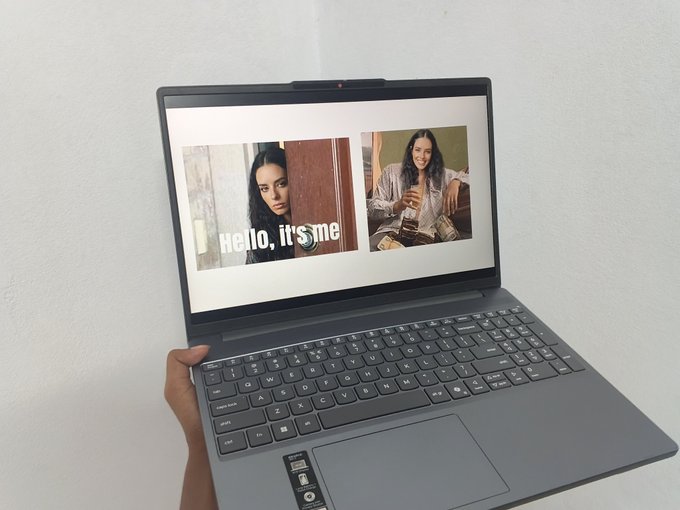 A person's hand holding an open ASUS laptop displaying a side-by-side comparison of photos labeled 'Hello, it's me' on a white background.