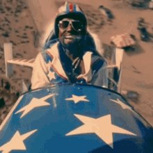 The image features a man wearing sunglasses and a helmet sitting inside a blue airplane with white stars on its side. The airplane has a "SPACESTOCKS MOMENTUM THAT GONNA OLAY HARD Today and yesterday, we got a big deep so get a bag of $asts $rdw $fly $nasa" caption that seems to be related to the post about the stock market. This caption suggests that there is a connection between the airplane's design and the stock market, possibly indicating some sort of investment theme or trend.