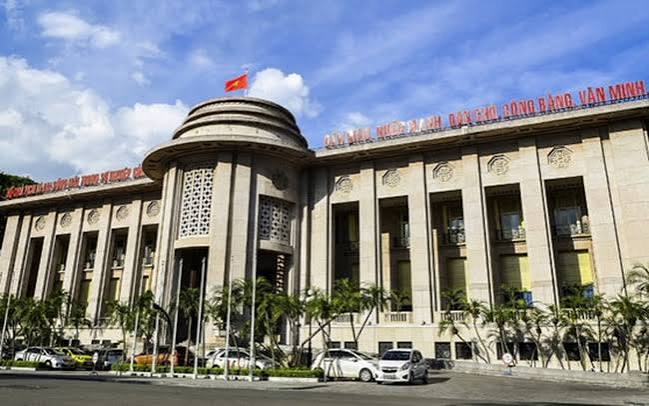 The State Bank of Vietnam building in Hanoi, featuring a Vietnamese flag on top and the slogan 'Xây dựng nước Việt Nam dân giàu, công bằng, văn minh' displayed on its facade.