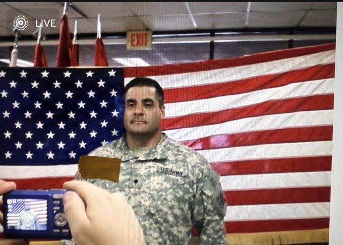 A 'LIVE' broadcast showing a U.S. Army soldier standing in front of a large American flag, while someone holds up a camera or phone in the foreground.