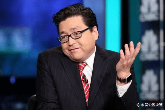 A man in a dark pinstripe suit with a red striped tie and glasses gesturing with his hand raised, appearing on what looks like a news program set, with watermark '吴说区块链' (Wu Says Blockchain).