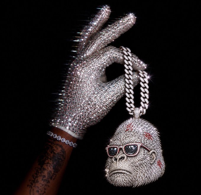 A diamond-encrusted jeweled glove holds up a large, sparkling pendant shaped like a gorilla wearing sunglasses.