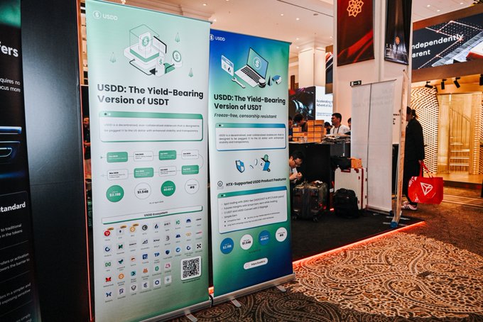 The image shows a large convention center with two banners hanging side by side. The banner on the left reads "Web3 Energy" while the one on the right says "USDD: The yield-bearing USDT version of UDS". These banners are displayed in front of a booth, possibly showcasing a new technology or product related to Web3 energy. In addition to these banners, there is also a poster with a logo and text that reads "Focus on what is in the image and how it relates to the post #IBW2026 IBW2026 is officially underway, and USDD is right in the heart of the action!".