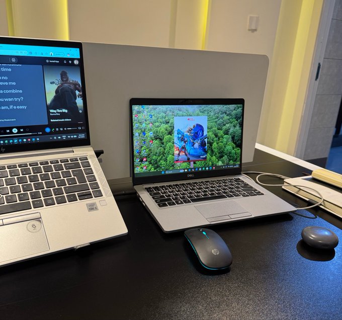 A desk setup featuring two open HP laptops, with the left screen displaying a song lyrics page and the right screen showing an aerial forest video, along with two wireless mice.