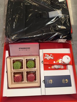 A Starbucks-branded Mid-Autumn Festival gift box from Tron, containing four mooncakes in green, red, and pink flavors, alongside promotional cards for "Moon Town" and other branded materials, with a black paper bag bearing the Tron logo visible in the background. The image shows the corporate Mid-Autumn gift that employees received, as referenced in the post's satirical commentary about working for Justin Sun's company.