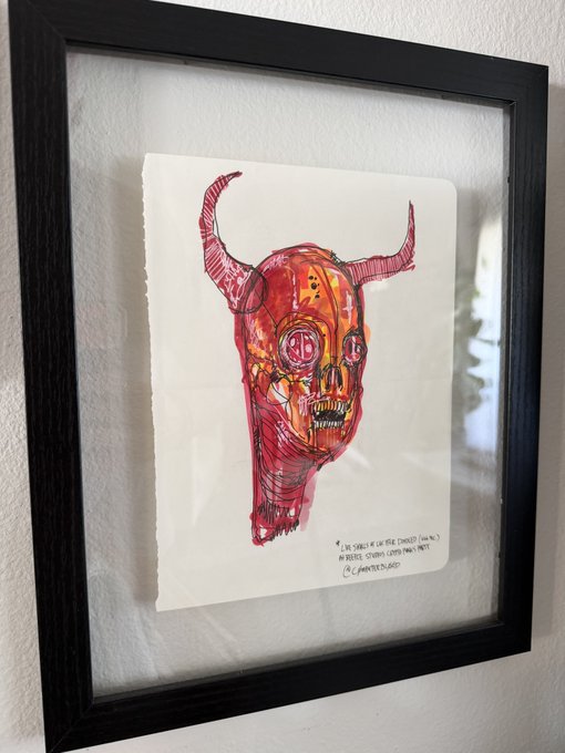 A framed watercolor and ink illustration of a horned demonic skull rendered in vivid reds and oranges hangs on a white wall, with handwritten text at the bottom reading "THE SKULL OF THE DEVIL," "MIXED MEDIA ON LOOSE PAPER," and what appears to be the title and artist signature, fittingly depicting the "666 Skulls of Lucifer" artwork mentioned.