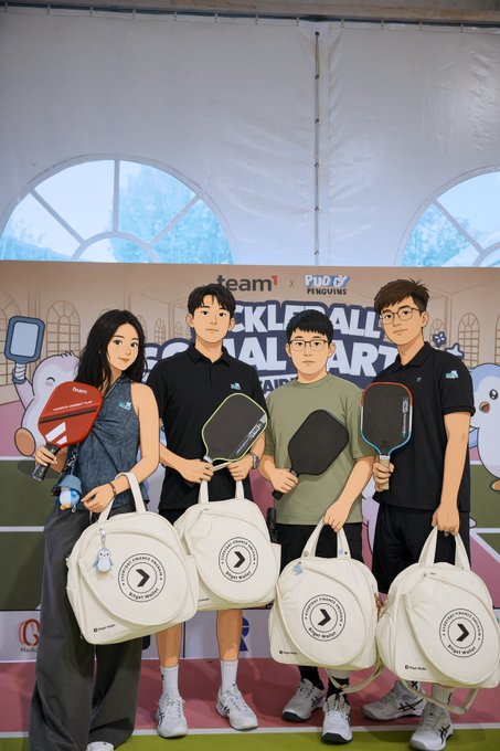 Four young people stand in front of a 'team1 x Pudgy Penguins PICKLEBALL FOR CHARITY' backdrop, holding pickleball paddles and white tote bags featuring a directional arrow logo.