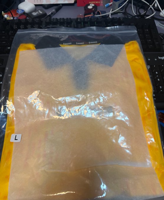 The image features a plastic bag with an open lid, likely containing a shirt or other clothing item, placed on top of a keyboard. The setting appears to be indoors, possibly at someone's home office or a computer desk. In the background, there is a computer monitor and a keyboard, further indicating that this scene takes place in a workspace or an area related to technology and computing tasks. The bag with its contents could potentially hold clothing items for work or other daily activities, but without more context, it is difficult to determine the exact purpose of the plastic bag within the image.