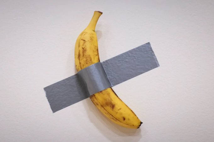 An artistic photograph of a yellow banana attached to a white wall with a strip of silver duct tape, reminiscent of Maurizio Cattelan's 'Comedian' artwork.