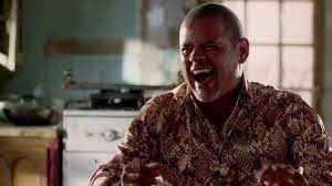 A man in a batik shirt laughs heartily while holding a glass, set against a dimly lit kitchen backdrop, evoking a sense of jovial anticipation. The image pairs with the caption "100k BTC 3200 ETH see u soon," amplifying the celebratory mood as the subject appears to be reacting to the optimistic crypto price predictions.