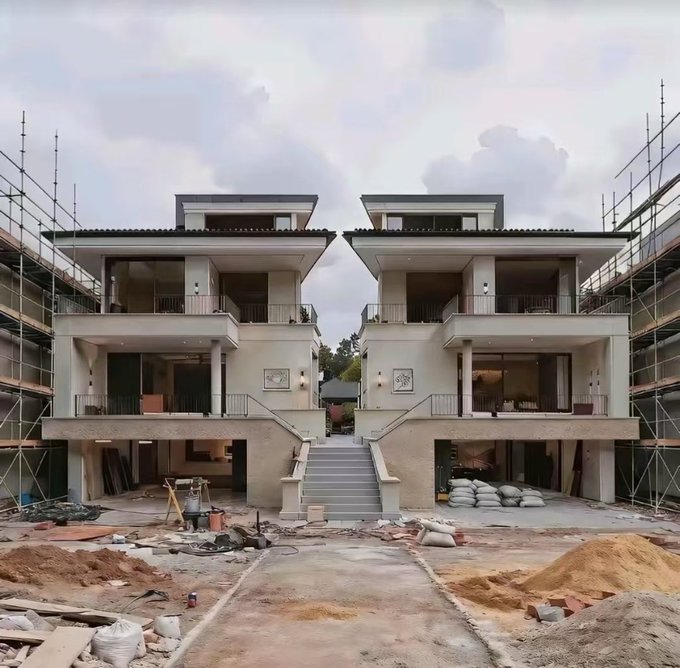 A symmetrical photo of two identical modern multi-story houses under construction, with scaffolding visible on both sides and a staircase in the center.