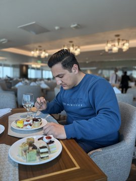 A man in a blue sweater enjoys a plate of assorted desserts in a well-lit dining room, with two tiered trays of pastries on the table. The image of someone leisurely savoring a meal contrasts with the post's focus on analyzing crypto price targets for ZEC, SOL, and BNB in 2026.