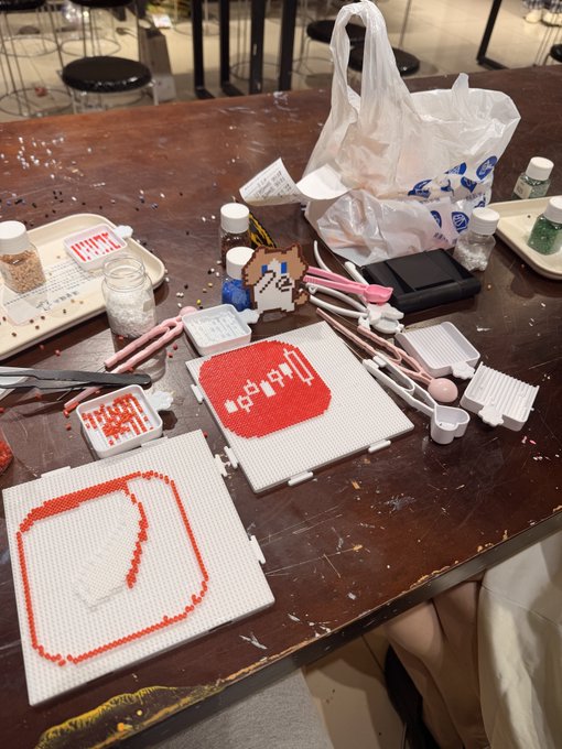 A tabletop scene of bead-art crafts featuring red and white beadwork designs, including a Minecraft heart icon and other pixel-art figures, alongside scattered bead containers, tools, and shopping bags — capturing the "Fake Build" of spinning up creative crafts instead of the "Real Build" of tracking Tonghuashun (同花顺) and Dongfang Caifu (东方财富) for stock market blessings.
