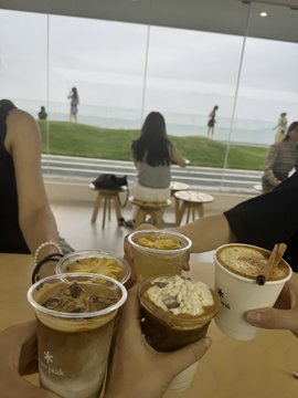 The image shows four cups of coffee being held by people who are standing around each other. The cups have different designs and colors, suggesting that they might be from various cafes or shops. The group appears to be enjoying their time together, possibly having a conversation while holding their drinks. The scene captures the essence of socializing and bonding over shared interests like coffee.