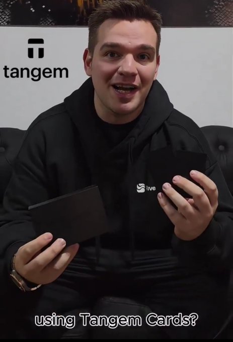 A man wearing a black '5ive' hoodie holding two black cards, with a 'Tangem' logo in the background and caption text reading 'using Tangem Cards?'.