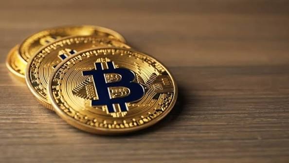 Two gold-colored Bitcoin tokens featuring the iconic "B" logo rest on a wooden surface, symbolizing the cryptocurrency that Michael Saylor's Strategy company has now sold in record amounts—3,588 BTC—marking a notable shift from his long-held "never sell" mantra.