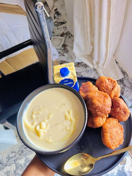 A meal served on a tray containing a bowl of creamy yellow custard or soup, a pile of fried dough balls, a packet of Magnolia milk, and a gold spoon.