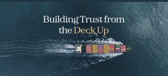 An aerial view of a container ship sailing on the ocean with the overlaid text 'Building Trust from the Deck Up'.