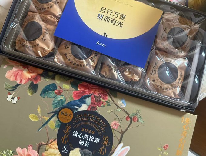 A box of HTX-branded Lava Black Truffle Custard Mooncakes (美心流心黑松露奶黄月饼) sits open, displaying individually wrapped mooncakes inside a decorative box featuring floral artwork, a bird, and the phrase "月行万里 翻而有光." The accompanying post humorously suggests that HTX (火币) is making money based on the quality of its Mid-Autumn Festival gift box, with the round moon symbolizing prosperity and growth.