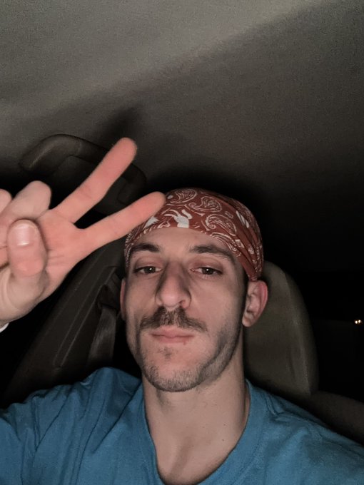A man wearing a red bandana poses with a peace sign in what appears to be a car.