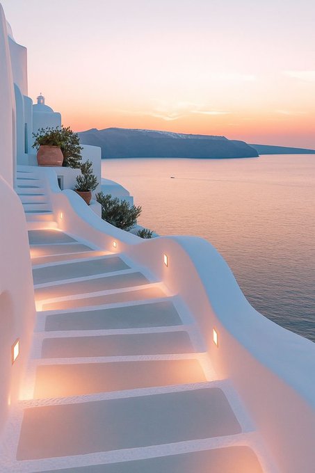 A scenic photograph captures the iconic white-washed architecture of Santorini, Greece, featuring curved staircases illuminated by warm lights leading down toward the Aegean Sea at sunset, with a small church bell tower visible on the left.