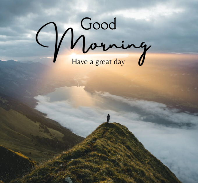 A scenic view of a person standing on a mist-covered mountain peak with sun rays breaking through clouds, overlaid with the text 'Good Morning Have a great day'.