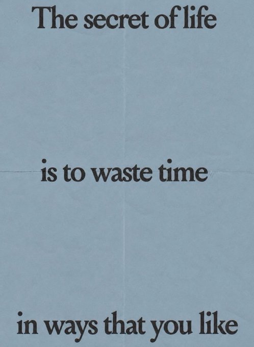 A light blue poster with black serif text reading 'The secret of life is to waste time in ways that you like'.