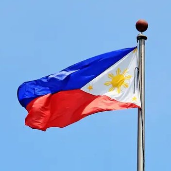 The flag of the Philippines waving on a flagpole against a clear blue sky, featuring its blue, red, and white design with a golden sun and three stars.