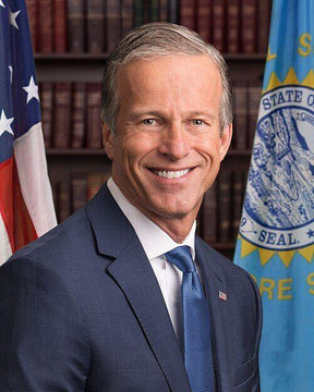Senate Majority Leader John Thune, pictured smiling in front of an American flag and a "Senate Seal" banner, plans to file cloture on the CLARITY Act motion to set up a September vote after the Senate returns from recess.