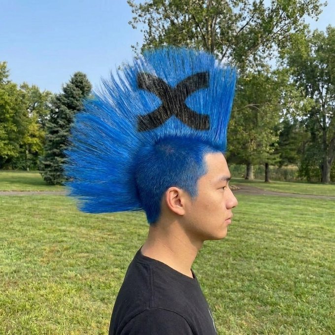 A young man with a striking tall blue mohawk featuring a black "X" design stands in profile against a grassy park backdrop, visually embodying the bold "100x becomes a lifestyle" mentality through his edgy, attention-grabbing hairstyle.