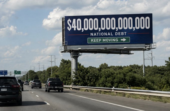 A billboard along a highway displays the U.S. "NATIONAL DEBT" at $40,000,000,000,000 with a "KEEP MOVING" sign beneath it, illustrating how quickly the country's debt is escalating toward the $50 trillion mark. The past milestone now feels distant given the rapid pace at which national debt continues to climb.
