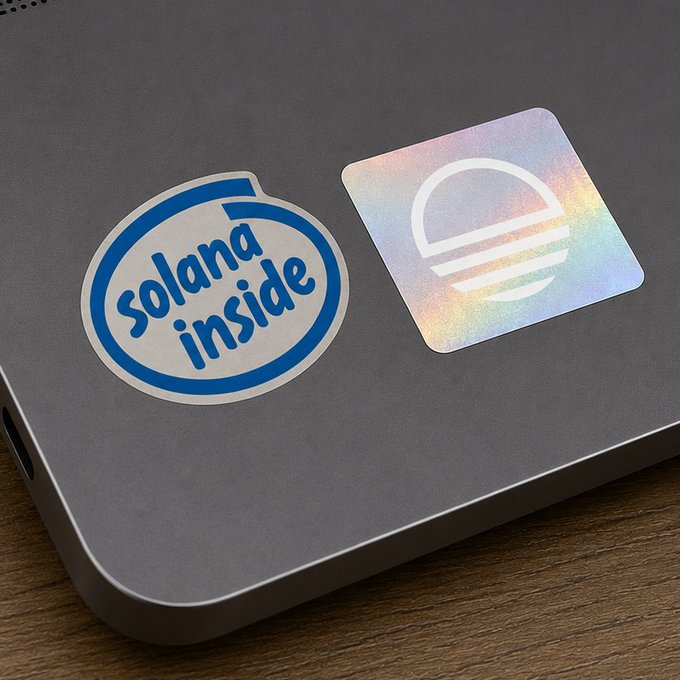 Two stickers on a silver laptop: a blue and white circular 'solana inside' sticker and a holographic square sticker featuring a stylized 'S' or hamburger-like logo.