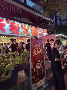 A crowd gathers at a bustling nighttime hotpot restaurant in Chengdu, with a prominent sign reading "火锅局" (Hotpot Gathering), tying into the post's playful mention of the Chengdu Hotpot Gathering. The lively street scene captures the social energy surrounding the event referenced in the caption.