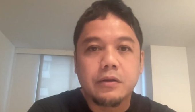 A man with dark hair and a goatee, wearing a dark shirt, speaks directly to the camera in a softly lit room with window blinds visible behind him, delivering the somber announcement about the sunsetting of the YGG Play Web3 game publishing unit.