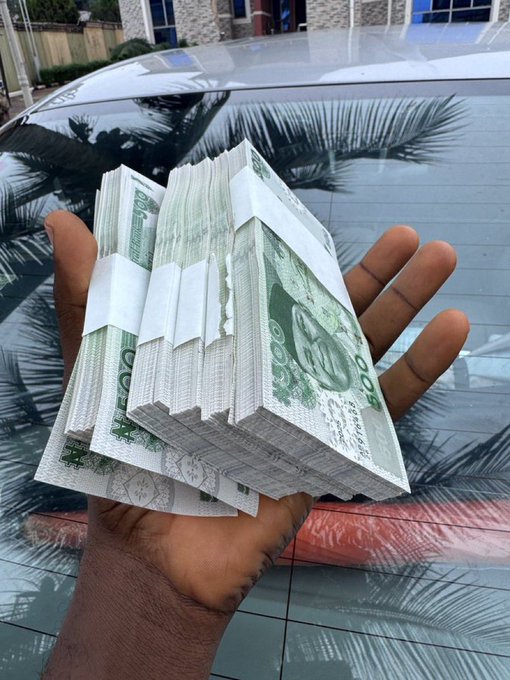 A hand holds several thick bundles of 100 denomination currency notes (appearing to be Nigerian Naira) against the backdrop of a car's windshield, illustrating the "Giveaway Time" theme by visually emphasizing the substantial amount of money being offered.
