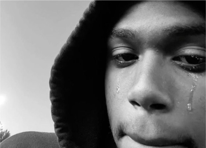 A black and white close-up portrait of a young person wearing a hood, with tears visibly streaming down their cheeks.