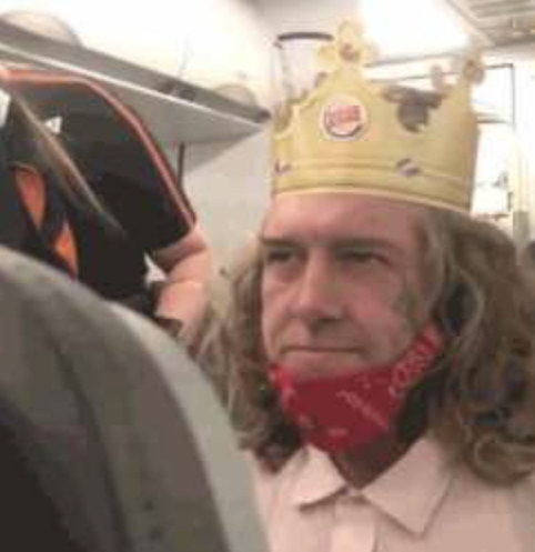 A widely-circulated meme image of a man wearing a Burger King paper crown and a red bandana as a face mask on an airplane, looking sideways with a stoic expression.