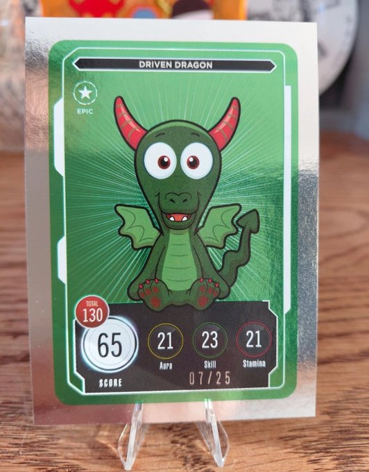 A trading card titled 'DRIVEN DRAGON' marked as EPIC, featuring a green cartoon dragon with red horns, showing a total score of 130, with breakdown stats of 65 Score, 21 Aura, 23 Skill, 21 Stamina, dated 07/25.