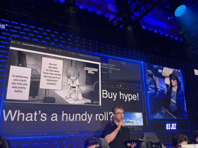 A man wearing glasses and a black polo shirt speaks into a microphone on a stage, standing before massive screens displaying "Buy hype! What's a hundy roll?" alongside an anime image of "Nurumi" and another screen labeled "03 JEZ." The hyperbolic crypto-aesthetic visuals and "hundy roll" terminology tie directly into the post's reference to "hyperliquid," as the speaker appears to be presenting or hyping the project in a flashy conference setting.