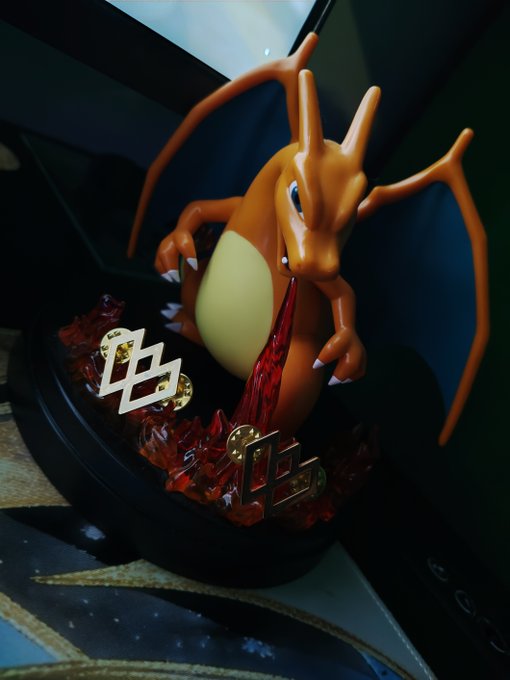 An orange Charizard figurine emerging from a Pokéball display with gold metallic emblems and red crystal-like effects.