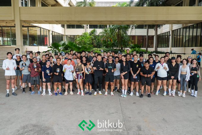 A large group of people poses for a team photo outside a building, with a 'bitkub Capital Group Holdings' logo displayed at the bottom.