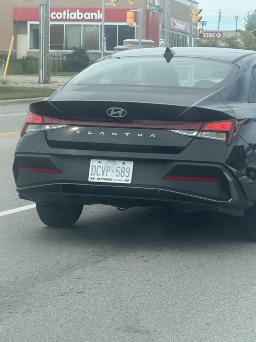 The rear view of a black Hyundai Elantra with an Ontario license plate (DCVP-589), parked in front of a Scotiabank and CIBC.