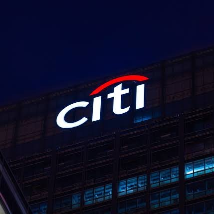 A nighttime photograph of an illuminated 'citi' logo on the side of a dark office building.