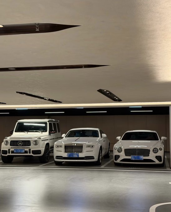 Three white luxury vehicles (a Mercedes G-Wagon, a Rolls-Royce, and a Bentley) parked side-by-side in a modern garage.