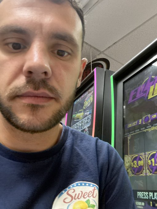 A man with a short beard takes a selfie while standing next to a slot machine displaying neon graphics and jackpot amounts of $3.00 and $11.